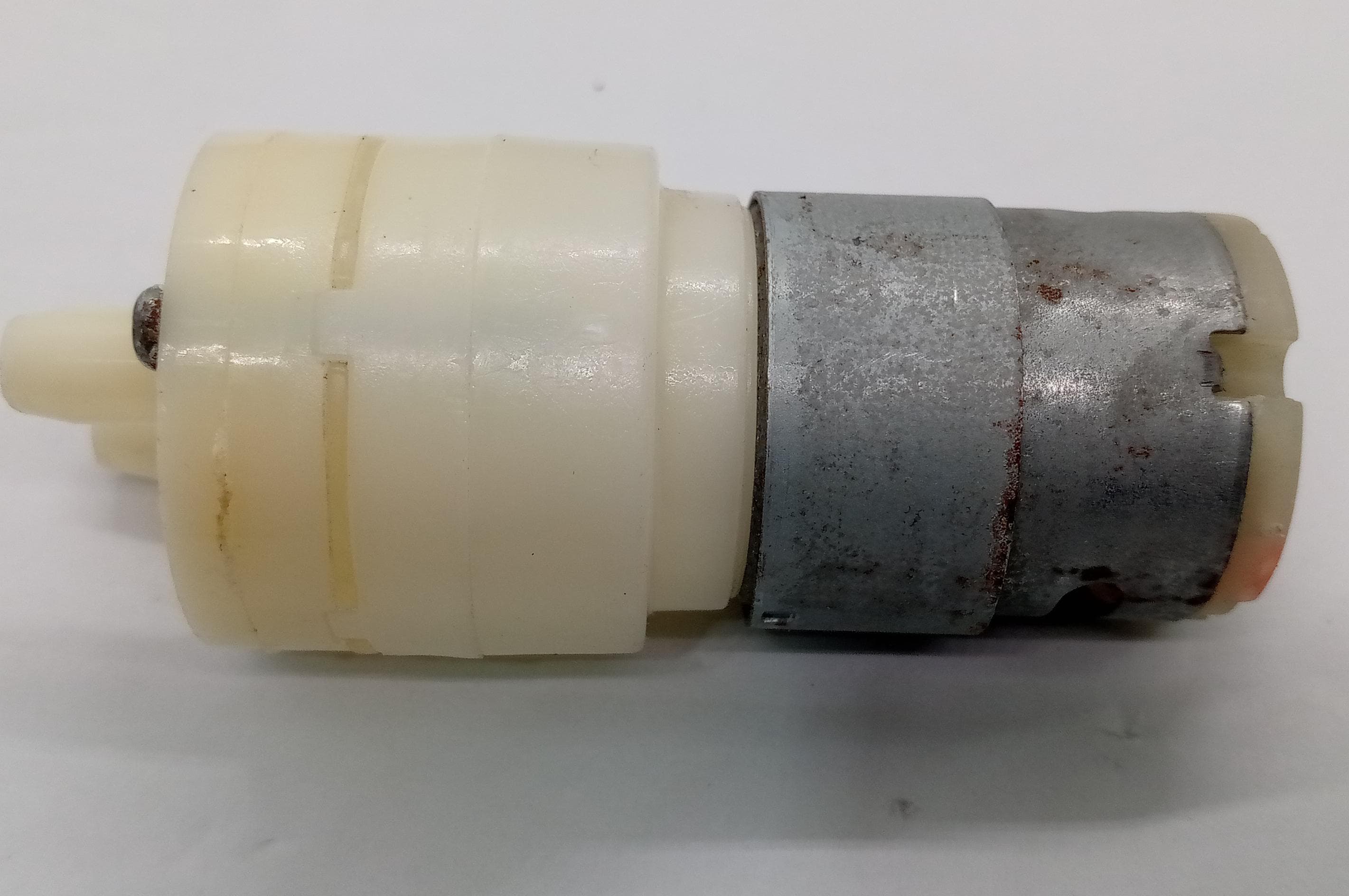12V Water Cooler Pump stock lot - a side-view of a small cylindrical white plastic pump head attached to a grey metal DC motor.