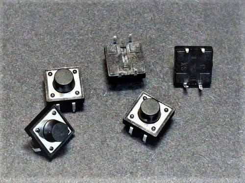12x12x9mm Tactile Push Button Switch - shown as a collection of five black square tactile switches with round push buttons on a dark grey surface.