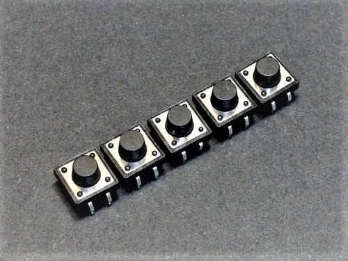 12x12x9mm Tactile Push Button Switch - a row of five square black tactile buttons with silver metal bases arranged diagonally on a grey surface.