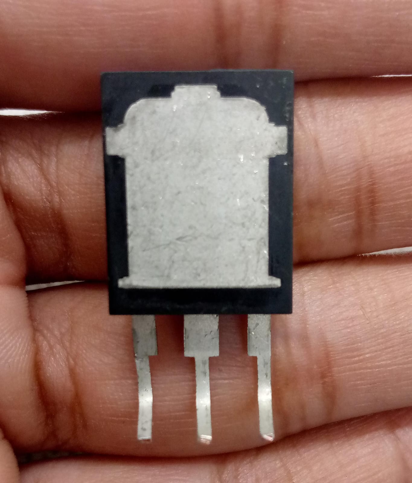 145A 650V MOSFET 145N65HS GF818 Chn - High-efficiency Power Transistor - a close-up of the back of a black electronic transistor component with three metal pins held in a hand.