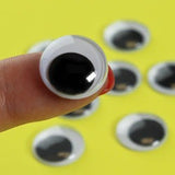15mm Googly Eyes 12pcs - a close-up of a single round plastic googly eye with a black pupil held on a finger against a yellow background.
