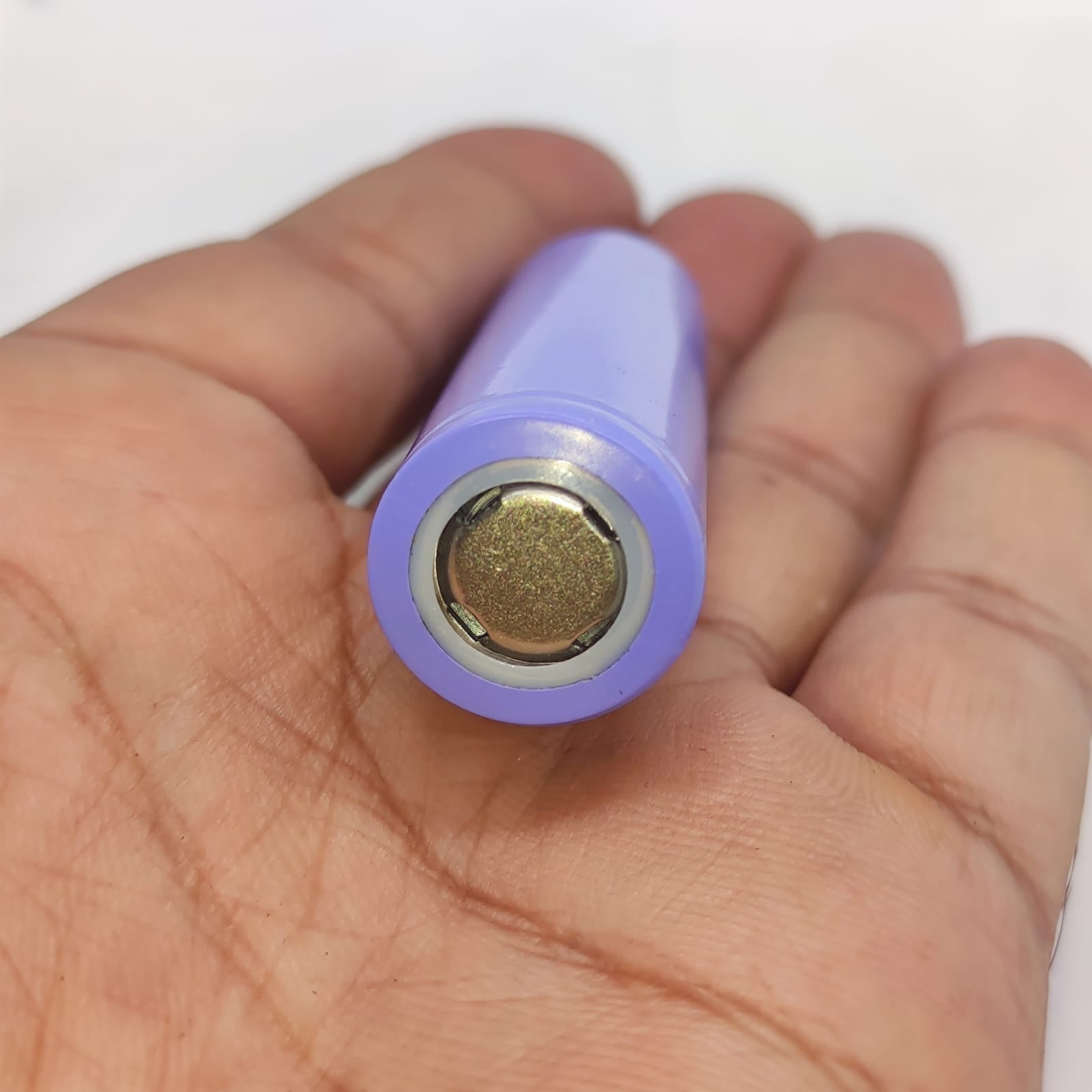 18650 Lithium Ion Cell refurb - a close-up view of the positive terminal end of a cylindrical purple battery held in a person's palm.
