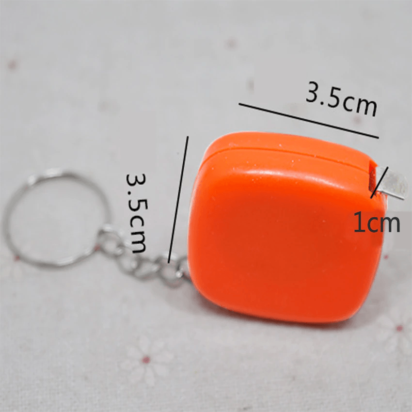 1m/ 3ft Pocket Size Inchies Tape And Measuring Tool - shown as an orange, square-shaped retractable tape measure keychain with dimension labels.