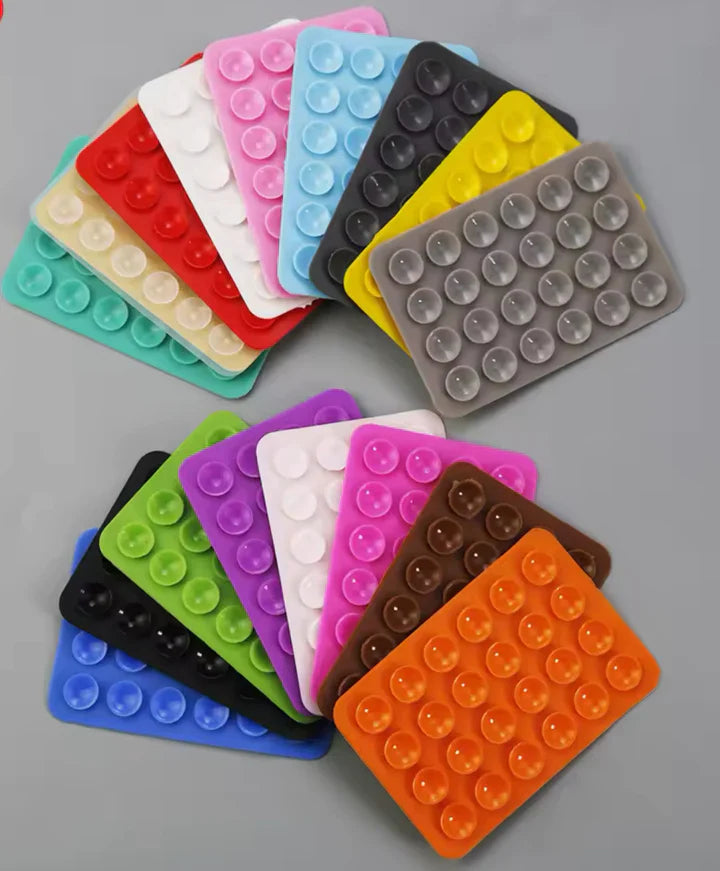 1pcs Silicone Suction Mobile Holder Pad - shown in a variety of rectangular, multi-coloured silicone mats featuring rows of small suction cups.
