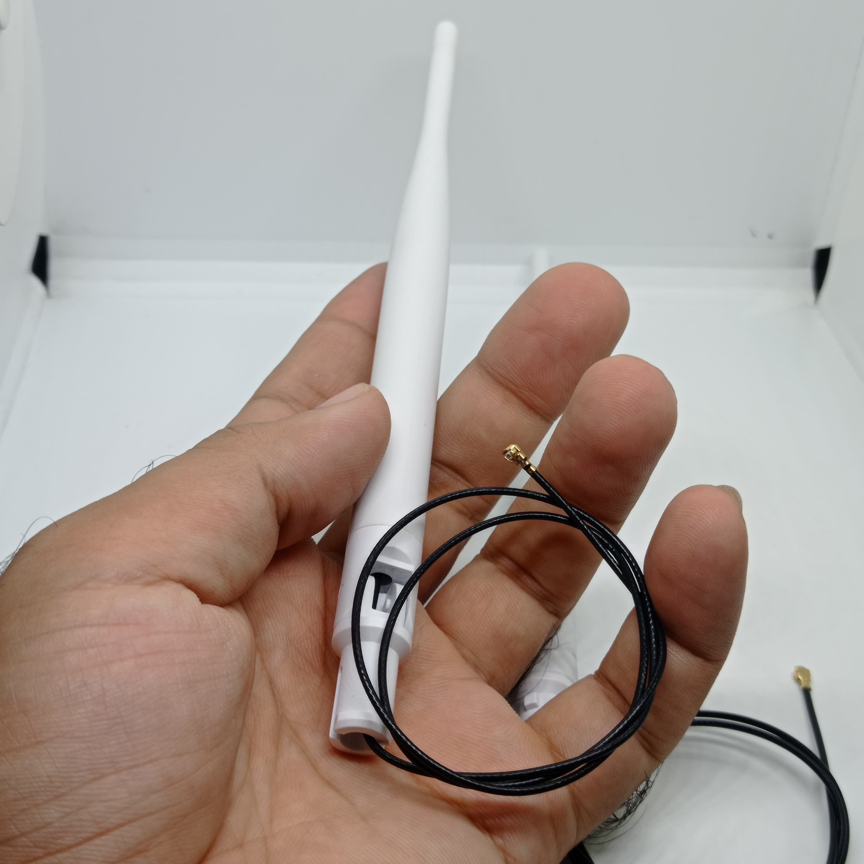 2.4GHz-5.8GHz 5db Wi-Fi Antenna With Ipex Connector - held in a hand, showing a white antenna with an attached thin black cable and a gold IPEX connector.
