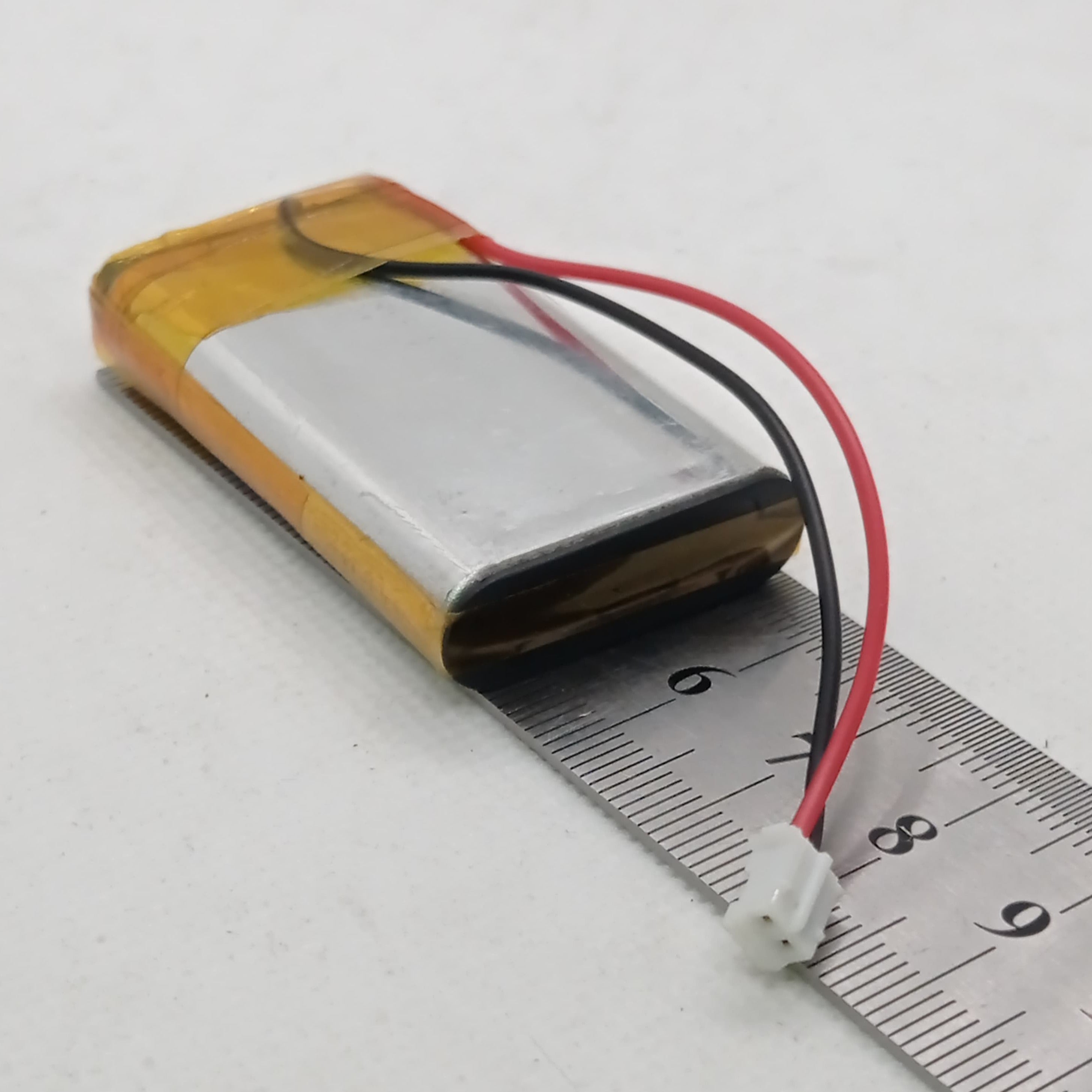 2000mAh 3.7V Lithium-ion battery - shown as a rectangular silver cell with yellow tape, red and black wires, and a white two-pin connector on a ruler.