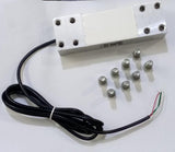 200kg Capacity Strain Guage Load Cell - a rectangular silver metal sensor with a black wire and eight small metal bolts arranged on a white surface.