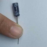 220 Uf 10V Through Hole Electrolytic Capacitor - a black cylindrical electronic component held by a finger, showing the printed 220uF 10V specifications.