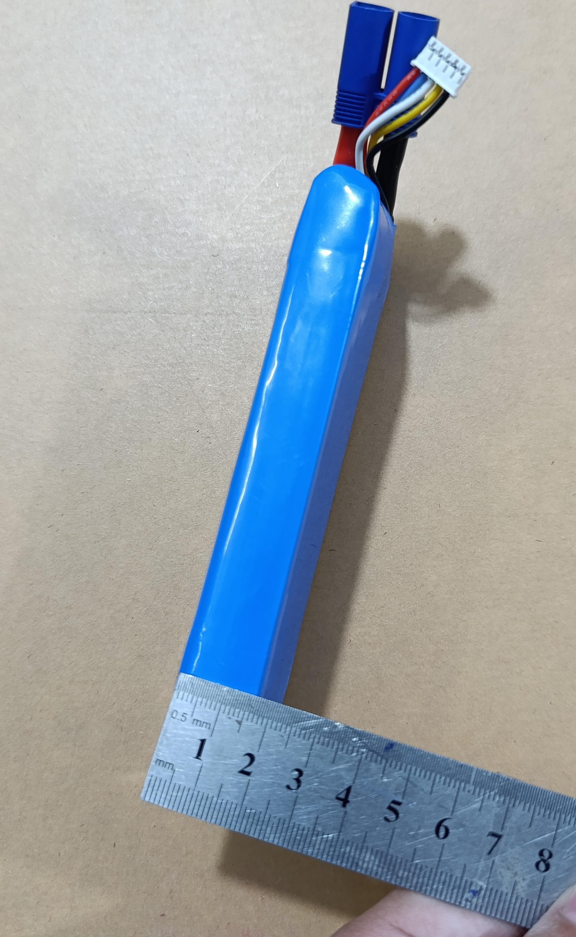 25S 4S 14.8V 2200mAh LiPo Battery - shown in a blue rectangular casing with a metal ruler measuring its width alongside a blue connector and white balance plug.