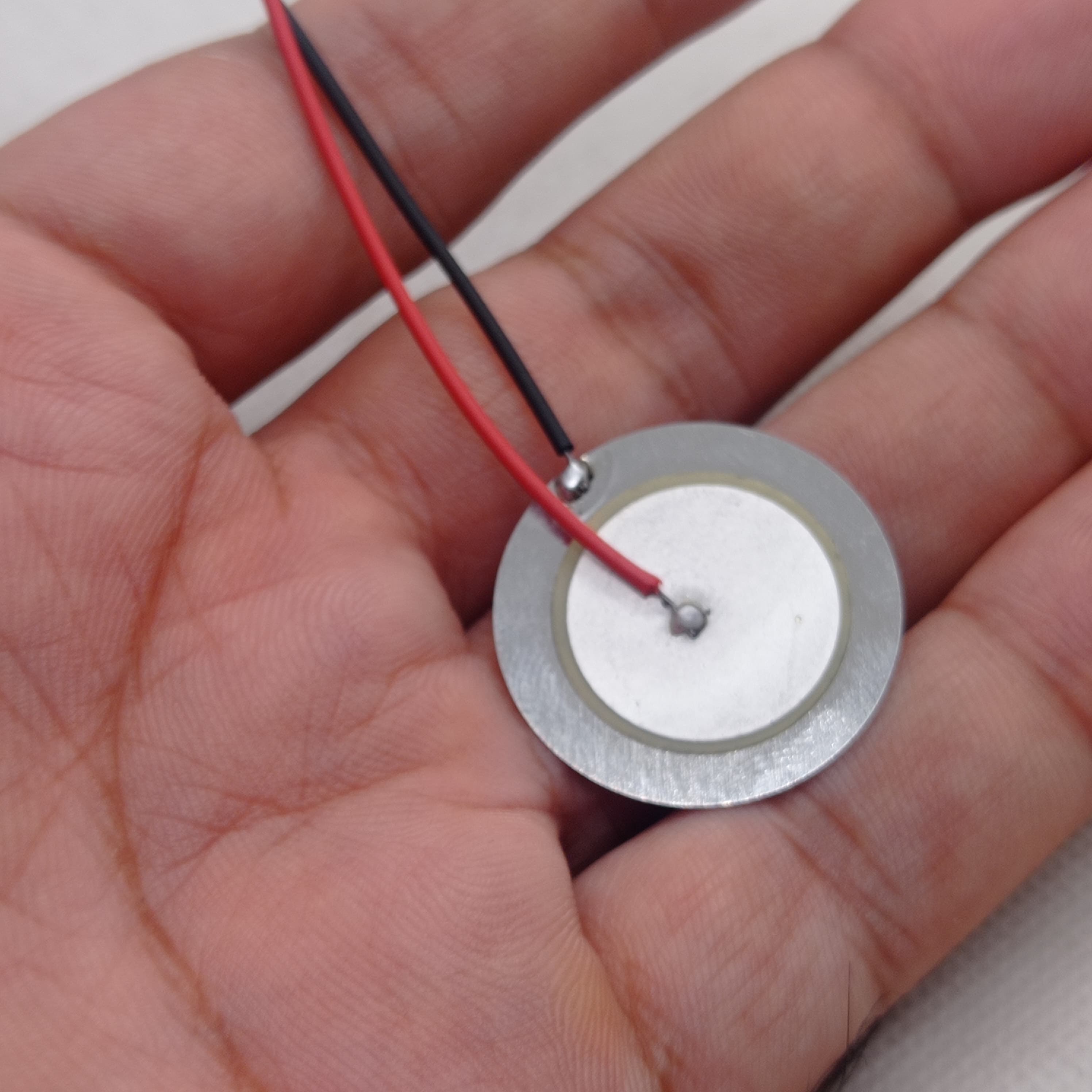 27mm Piezoelectric Ceramic Disc Piezo Element Plate With Wires - shown as a round silver metal disc with a white ceramic center and attached red and black wires.
