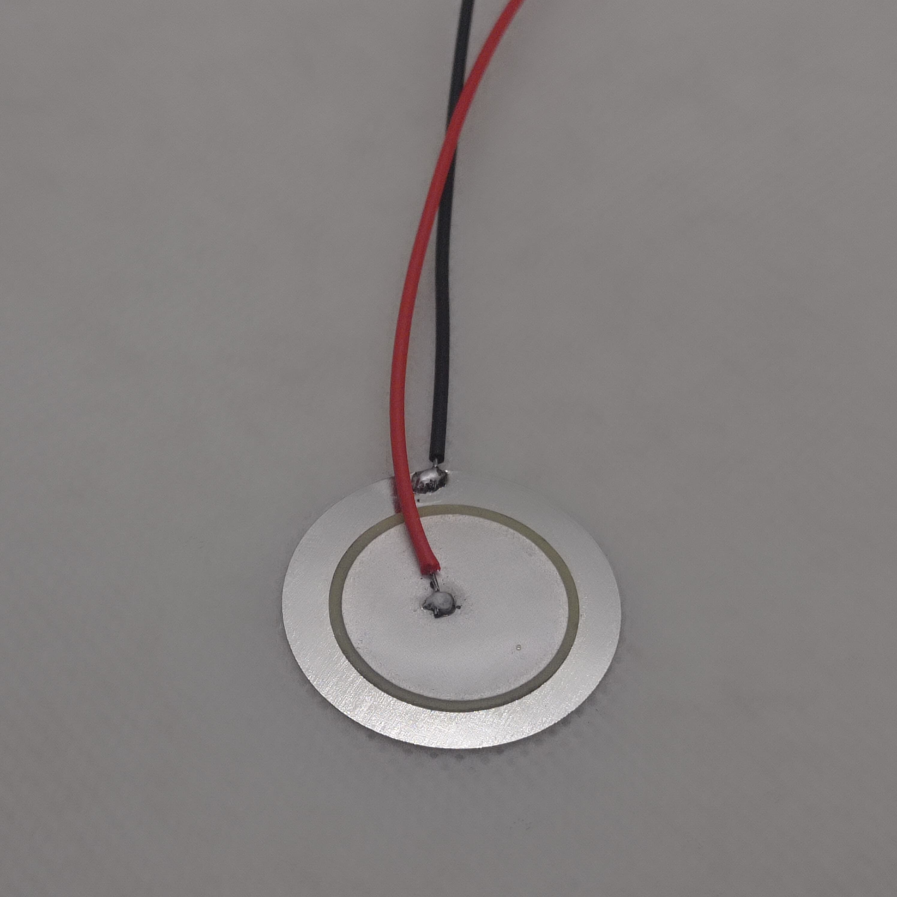 27mm Piezoelectric Ceramic Disc Piezo Element Plate With Wires - a circular silver metal disc with a ceramic center and attached red and black wires.