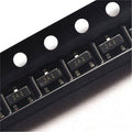 2N3906 MMBT3906 Transistor PNP SMD Sot-23 - shown in a close-up view of multiple black components arranged in a plastic carrier tape.