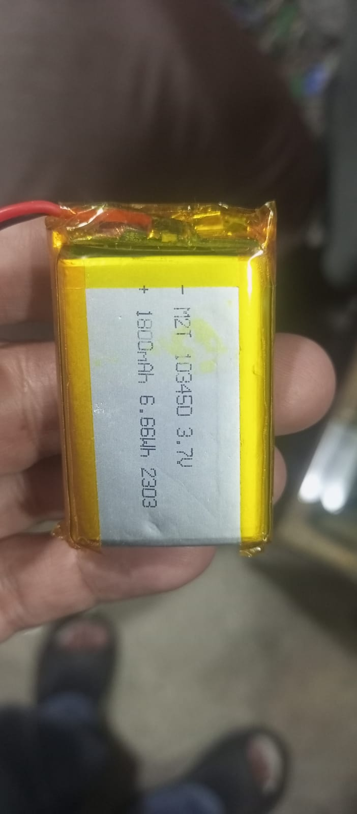 3.7V 1800mAh Lithium Battery With BMS - rectangular yellow-wrapped lithium-ion battery held in a hand, showing printed text including 103450 3.7V.
