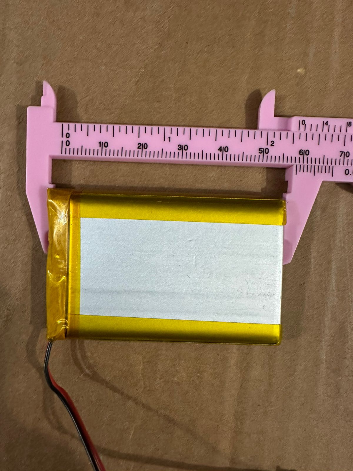 3.7V 2500mAh Lithium-Ion Rechargeable Battery - Li-Po Battery Pack - a rectangular gold-wrapped battery with two wires being measured by a pink plastic vernier caliper.