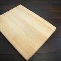300MMX400MMX10MM wood project board - a rectangular, light-colored wooden board placed diagonally on a dark, horizontal-planked wooden surface.