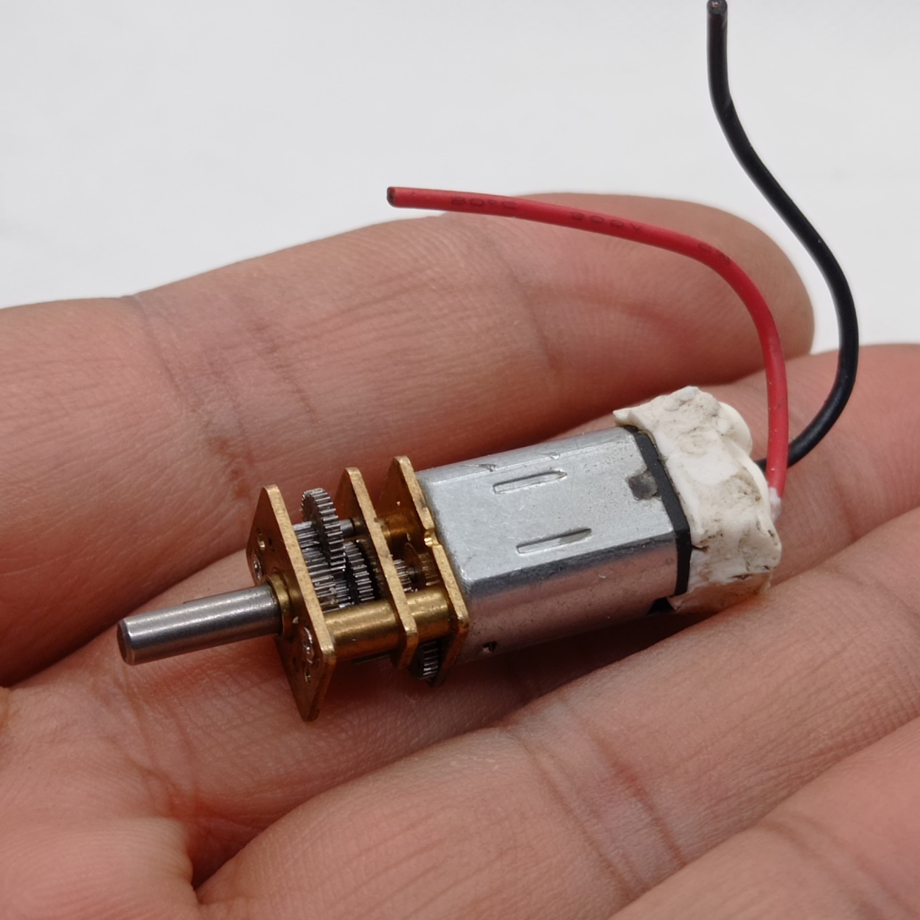 300RPM N20 DC Gear Motor The Perfect Low RPM High Torque Motor For Your Electronics Projects - held in a hand, showing a silver metal motor body, a brass gearbox with exposed gears, a metal output shaft, and two wires.