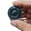 32 ohm 0.1W speaker - a close-up of a small, round, black speaker with a ridged diaphragm held between a person's thumb and index finger.