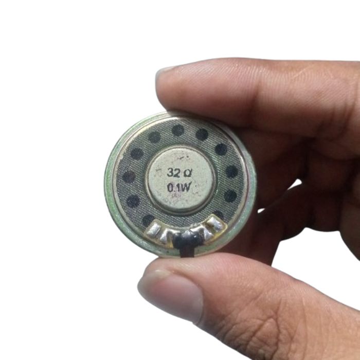 32 ohm 0.1W speaker - a small circular metal component held by a hand, showing the printed text "32 Ω" and "0.1W" on its back surface.