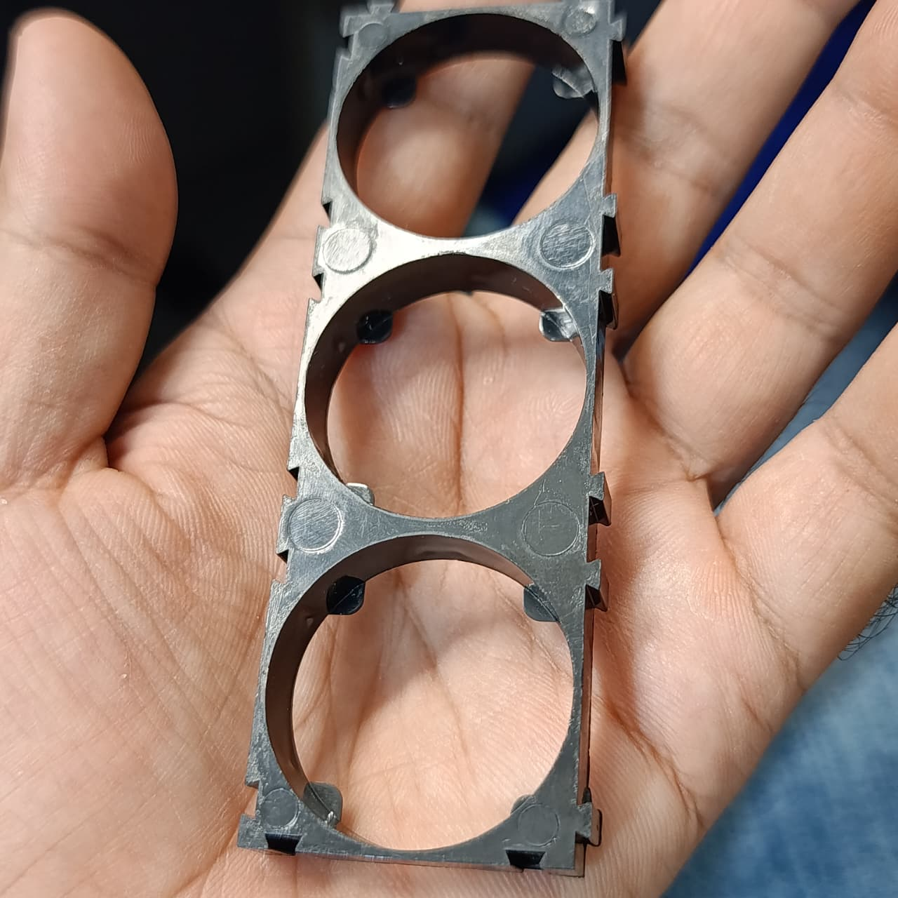 32700 Lithium Cell Holder Bracket - 3P Triple Cell Spacer - shown as a black, rectangular plastic frame with three circular cutouts held in a hand.