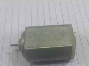 390PA DC Motor - shown as a silver-colored cylindrical motor with a small metal shaft extending from the front, resting on lined paper.