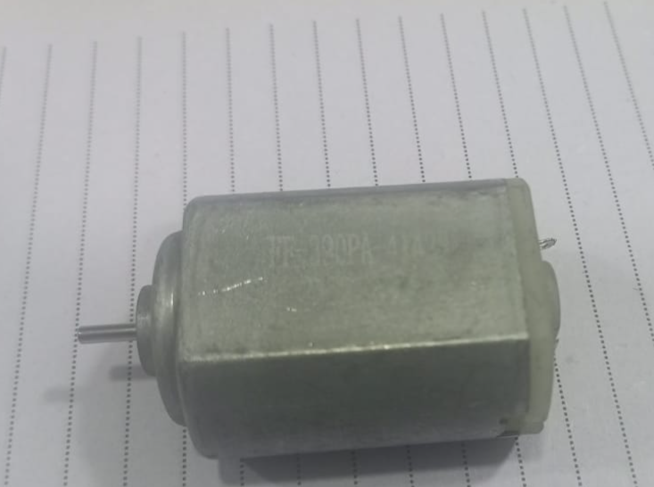 390PA DC Motor - shown as a silver-colored cylindrical motor with a small metal shaft extending from the front, resting on lined paper.