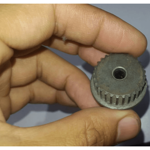 3mm Timing Pulley P28 - a close-up view of a grey, circular, toothed timing pulley with a center hole, held between a person's fingers.