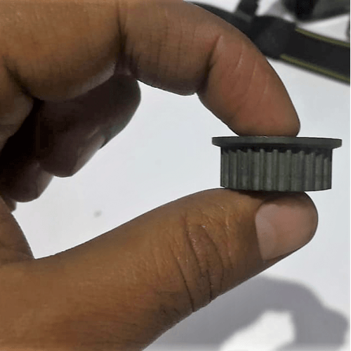 3mm Timing Pulley P28 - a close-up shot of a small, grey, cylindrical toothed pulley held between two fingers.