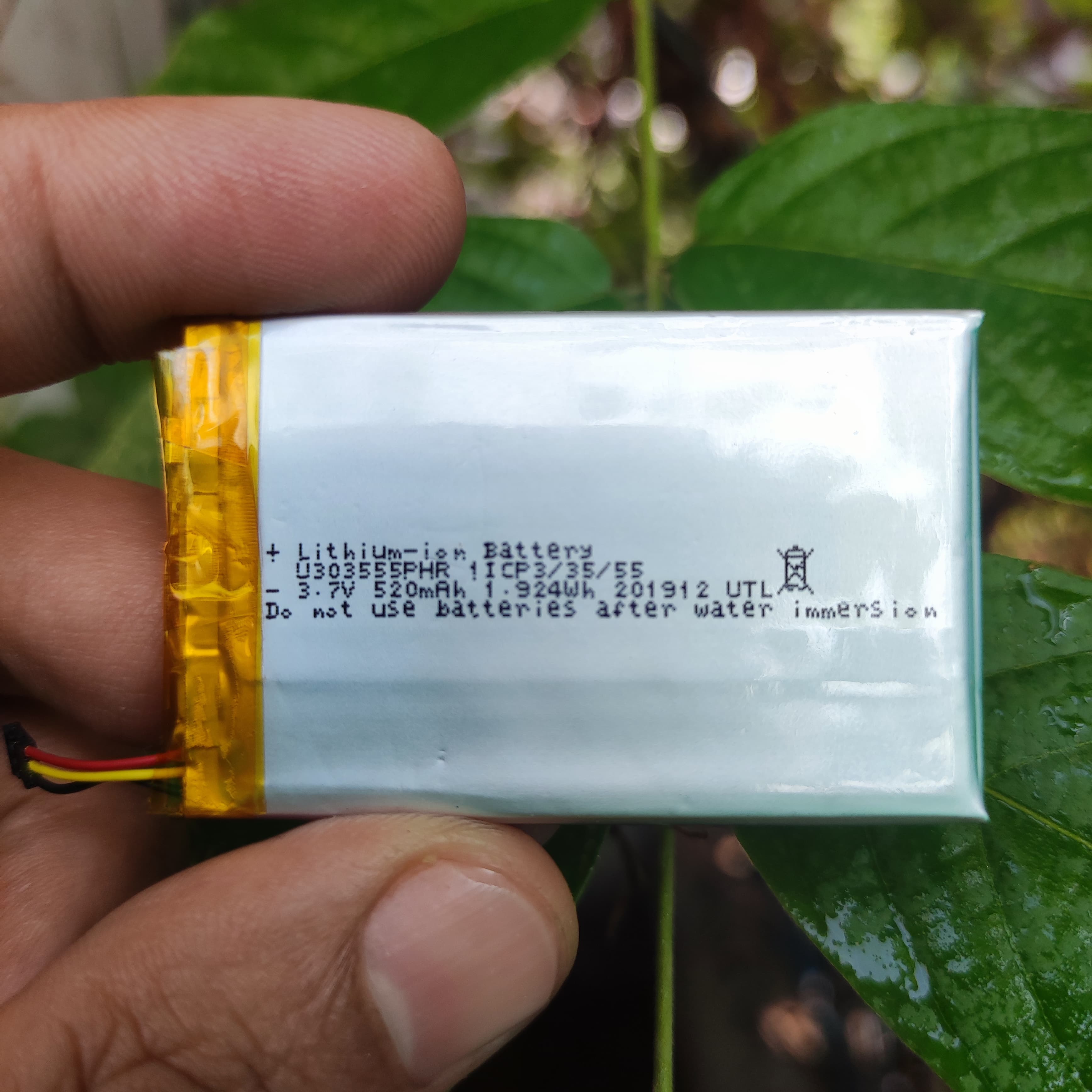 3mm x 35mm x 55mm 3.7V 500mAh Lithium Polymer Rechargeable Battery - a rectangular silver battery with yellow tape and red, black, and yellow wires held in a hand.