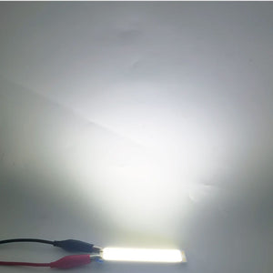 3W 3.7V 1000mA 300LM LED COB Light Module For Bike DIY Work Lamp Buy - a rectangular white LED strip illuminated and connected to red and black alligator clip wires.
