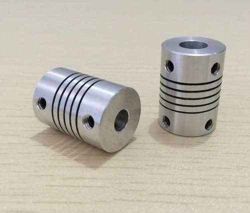 3x6.35mm Flexible Coupling Shaft - two silver cylindrical metal couplers with spiral cut-outs and side set-screw holes on a light wooden surface.