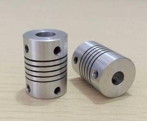 3x6.35mm Flexible Coupling Shaft - two silver cylindrical metal couplers with spiral-cut flexible bodies and set screw holes on a wooden surface.