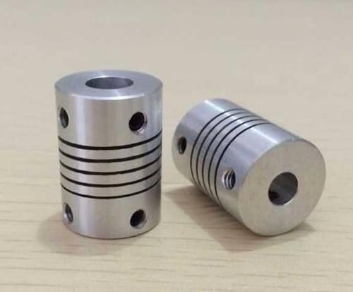 3x6.35mm Flexible Coupling Shaft - two silver cylindrical metal couplers with spiral-cut flexible bodies and set screw holes on a wooden surface.
