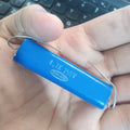4.7k 250V capacitor - a blue cylindrical electronic component with two wire leads, held in a hand above a computer keyboard.