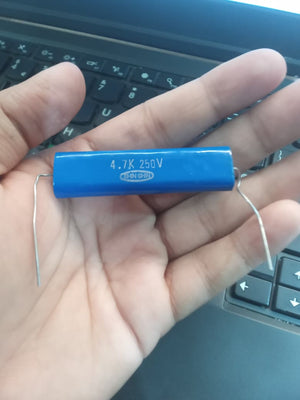 4.7k 250V capacitor - a blue cylindrical electronic component with wire leads held in a hand over a laptop keyboard.