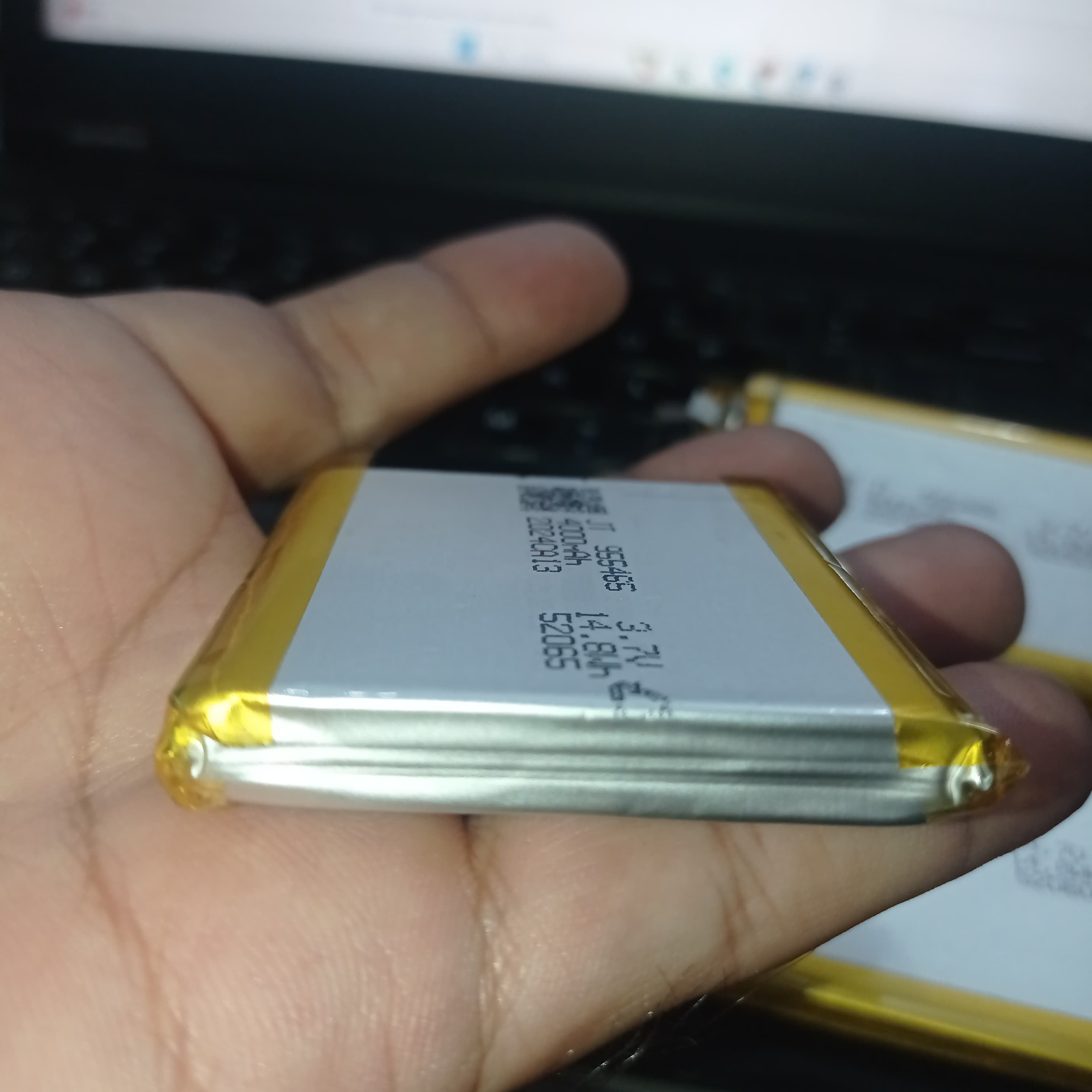 4000mAh 3.7V Lithium Ion Battery Price 9.5mm X 54mm X 65mm - a close-up shot of a rectangular silver battery with yellow tape edges, showing printed text including 955465 and 14.8Wh.