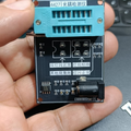 44271 Optocoupler Tester - Photocoupler Testing Module With ZIF Socket - a black circuit board with a blue ZIF socket, a DC power jack, and text labels in Chinese, held in a person's hand.