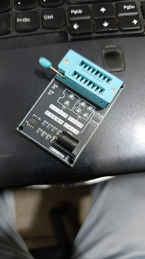 44271 Optocoupler Tester - Photocoupler Testing Module With ZIF Socket - a black circuit board with a blue ZIF socket, a buzzer, and Chinese text labels, resting on a laptop keyboard.