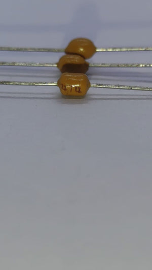 474 Multilayer Ceramic Capacitor resistor type - close-up shot of three small, yellow, axial-leaded components with the text "472" printed on the body.