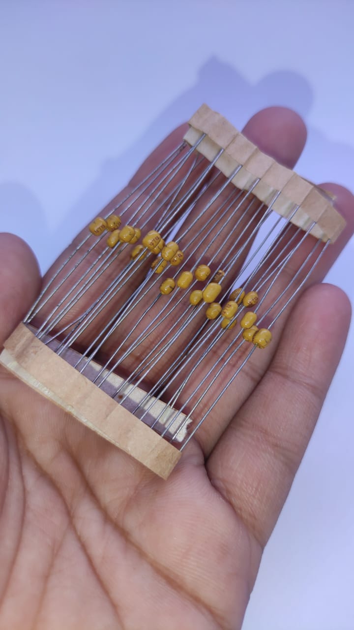 474 Multilayer Ceramic Capacitor resistor type - a strip of small, yellow, axial-leaded capacitors held together by two parallel paper tapes and held in a hand.