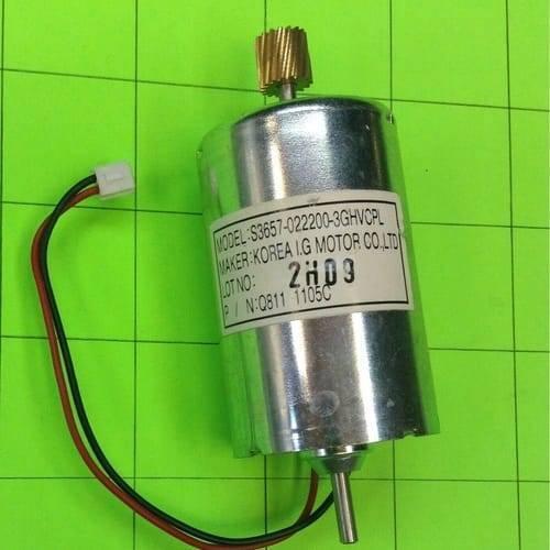 5 To 26V DC Motor Lot - a silver cylindrical DC motor with a brass gear on top, a bottom shaft, and a two-wire connector on a green grid.