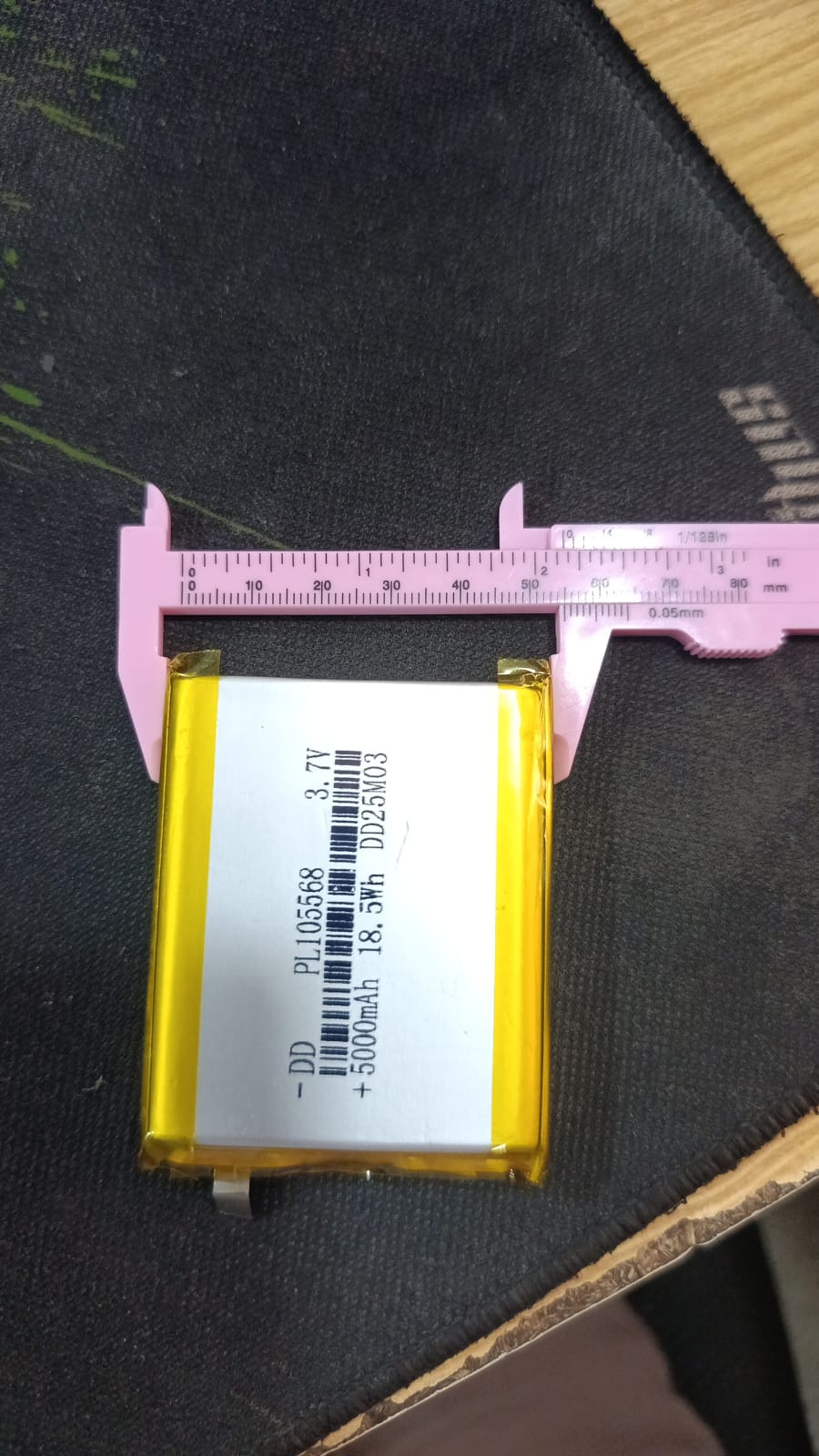 5000mAh 3.7V Lithium Ion Battery Price - a rectangular silver and yellow cell being measured for width with pink plastic calipers on a dark surface.