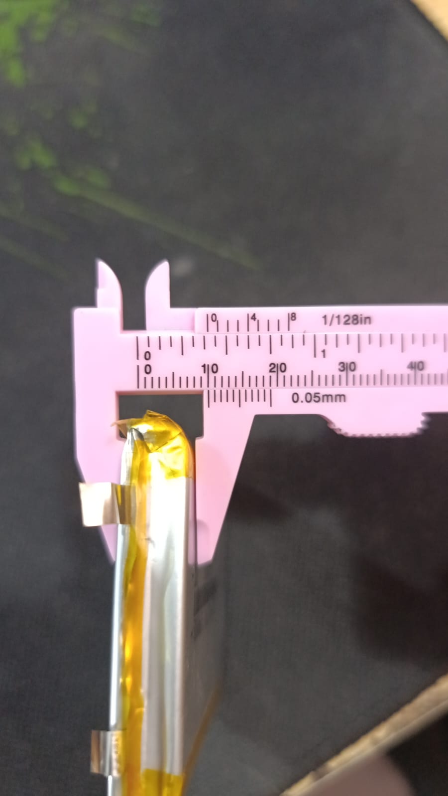 5000mAh 3.7V Lithium Ion Battery Price - a close-up shot showing the silver and yellow battery being measured by a pink plastic vernier caliper.