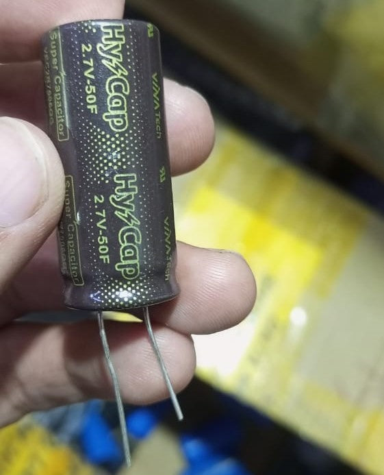 50F 2.7V Capacitor - a brown cylindrical supercapacitor with two metal leads held between fingers, showing Hy-Cap branding and specifications.