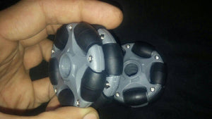 58mm Omni Wheel Universal Wheel - shown as a close-up of two grey plastic wheels with small black rollers held in a hand against a black background.