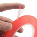 5mm 5 Meter Transparent Adhesive Double Sided Tape For Mobile LCD & Touch Screen - a hand holding a roll of red-backed adhesive tape with a partially peeled clear liner.