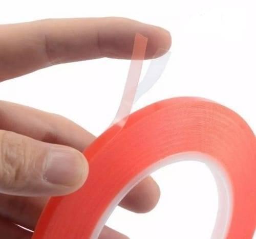 5mm 5 Meter Transparent Adhesive Double Sided Tape For Mobile LCD & Touch Screen - a hand holding a roll of red-backed adhesive tape with a partially peeled clear liner.