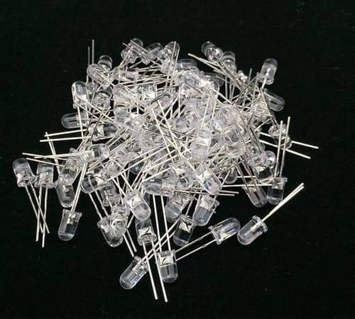 5mm White LED Light Bulb - a large pile of clear, round-top light-emitting diodes with two metal pins each on a black background.