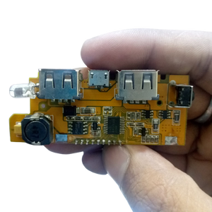 5V 2A DIY Power Bank Module With Display And Emergency Light Points - held in a hand, showing a yellow circuit board with two USB ports, a micro-USB port.