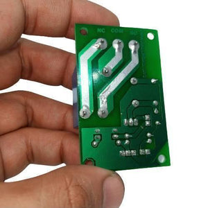 5V 30A Relay Module SLA-05VDC-SL-C - shown from the bottom side, held by a hand, displaying the green PCB, solder joints, and NC, COM, and NO terminals.