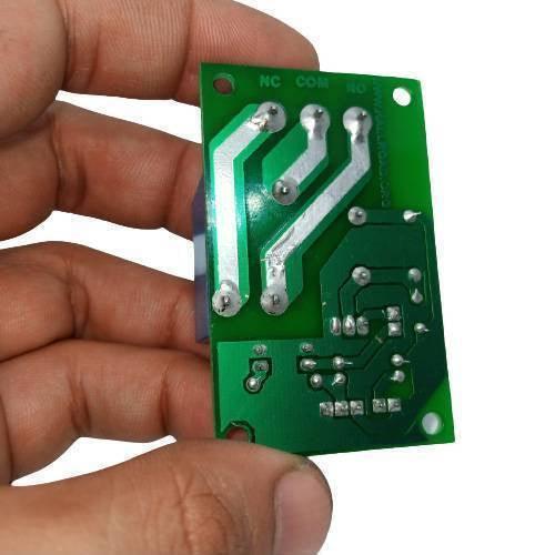 5V 30A Relay Module SLA-05VDC-SL-C - shown from the bottom side, held by a hand, displaying the green PCB, solder joints, and NC, COM, and NO terminals.